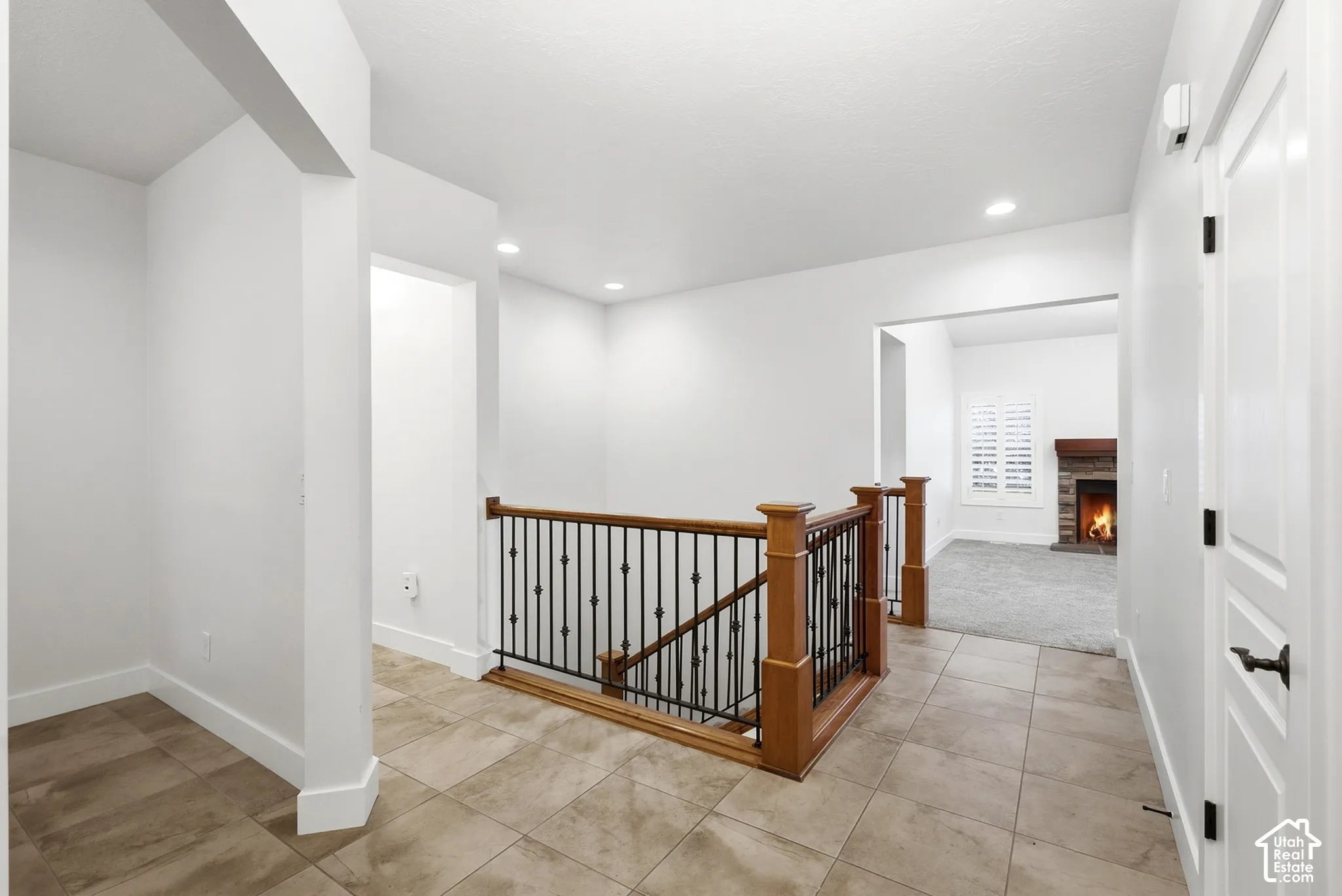 Tiled flooring throughout, staircase with wood banister and wrought iron spindles, recessed ceiling lighting, white interior doors with matte black hardware, and a stone fireplace with wood mantel
