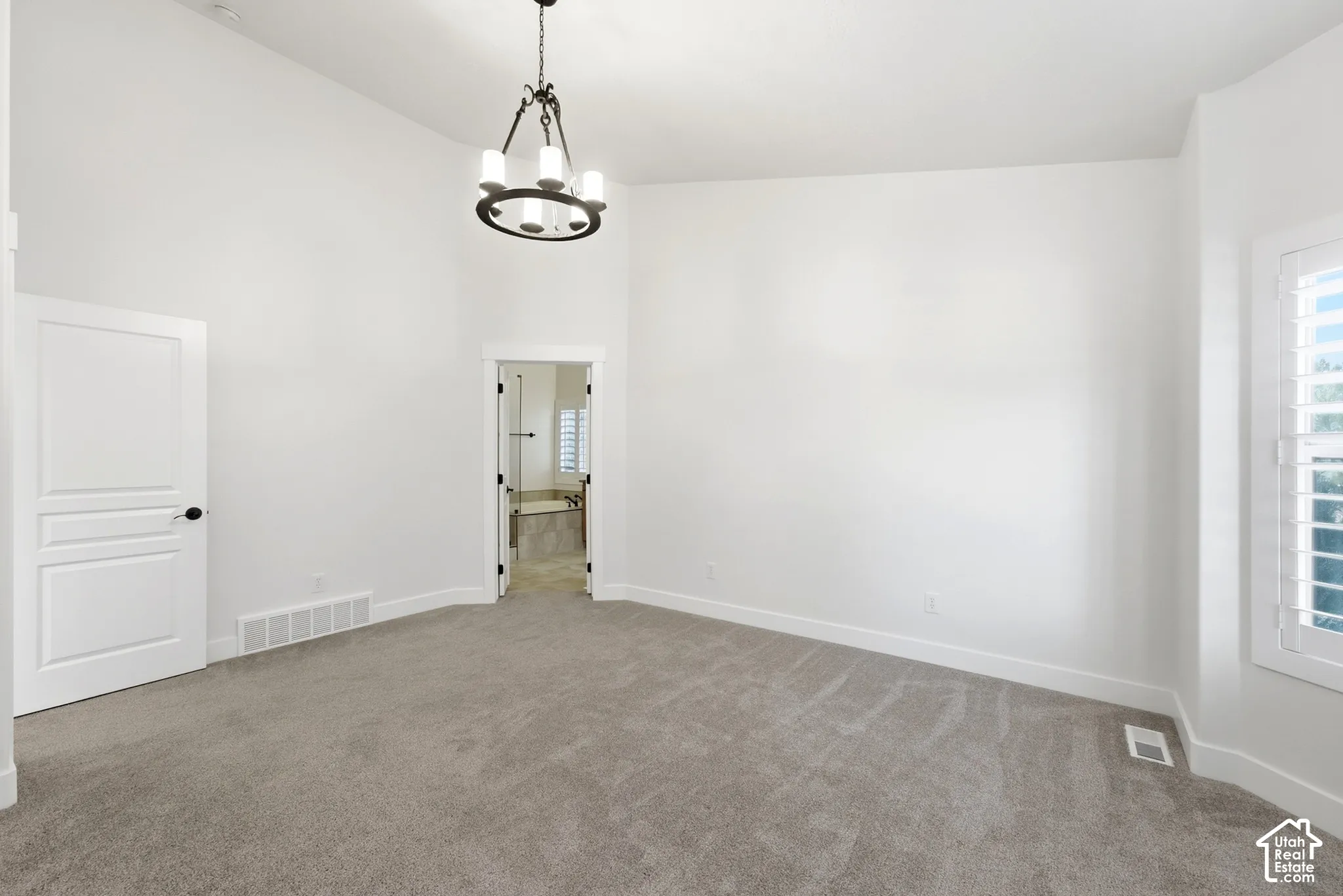 Plush carpeting, a modern chandelier, white interior shutters, and a white paneled door with black hardware