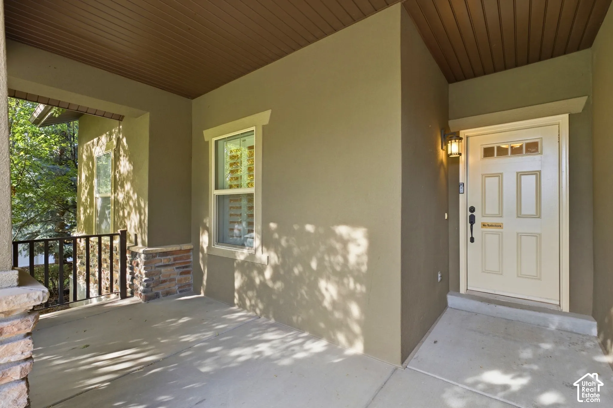 Covered porch entry featuring a wood-panel ceiling, sconce lighting, and a paneled entry door with transom windows