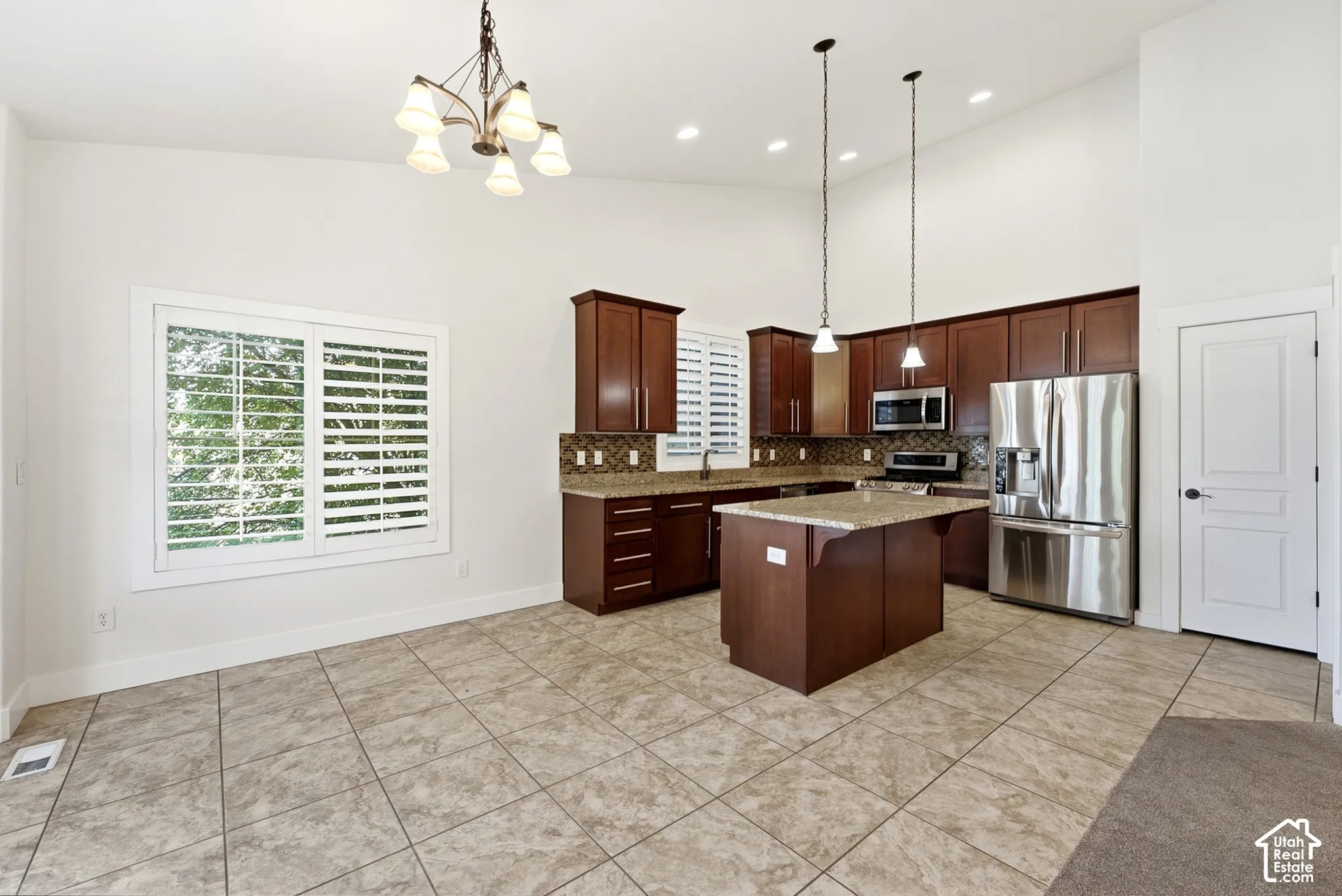 Vaulted ceilings with recessed lighting, tile flooring, rich wood cabinetry, stainless steel appliances, and a center island