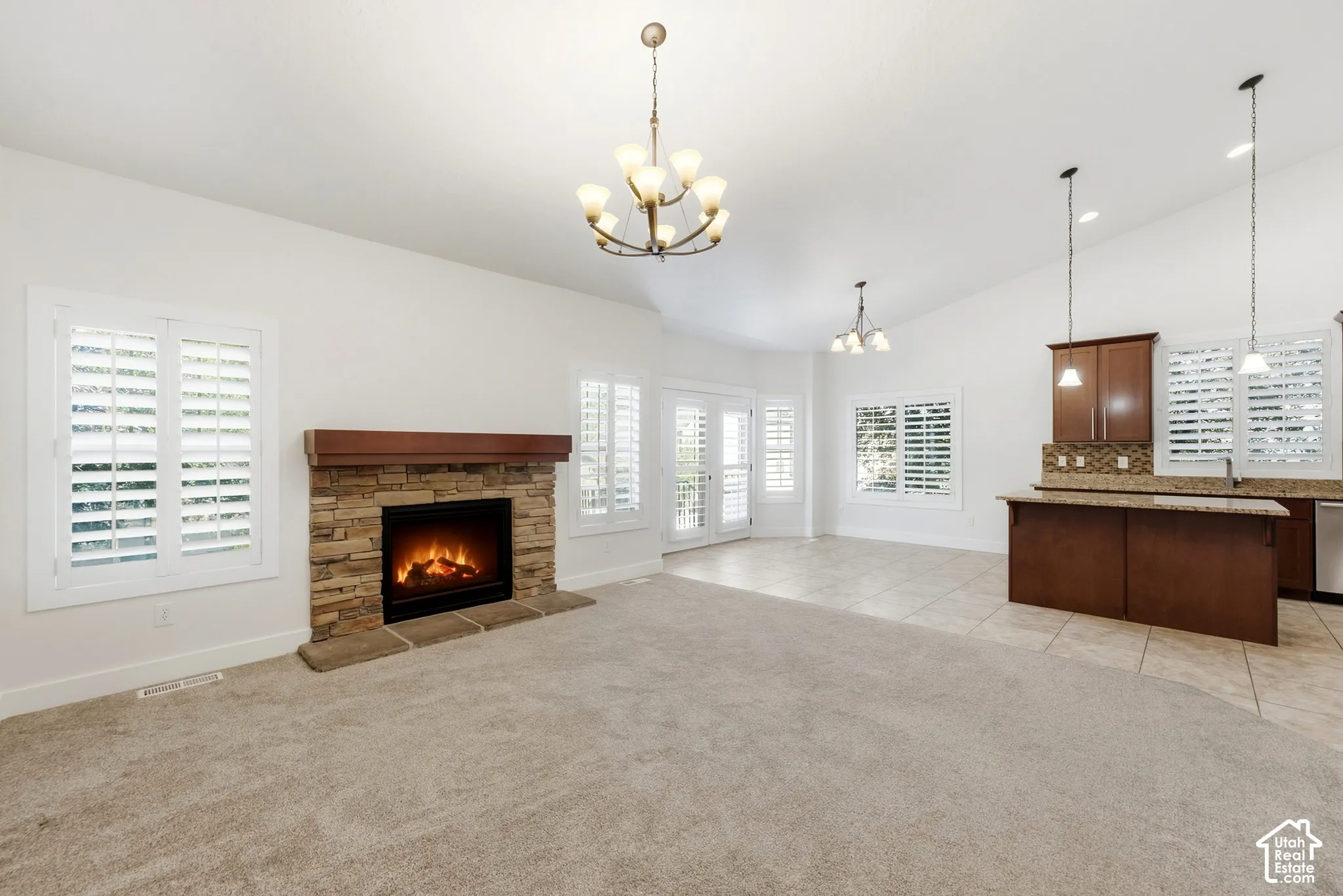 Stacked stone fireplace with a wood mantel, vaulted ceilings, plantation shutters, French doors, and a kitchen island with pendant lighting