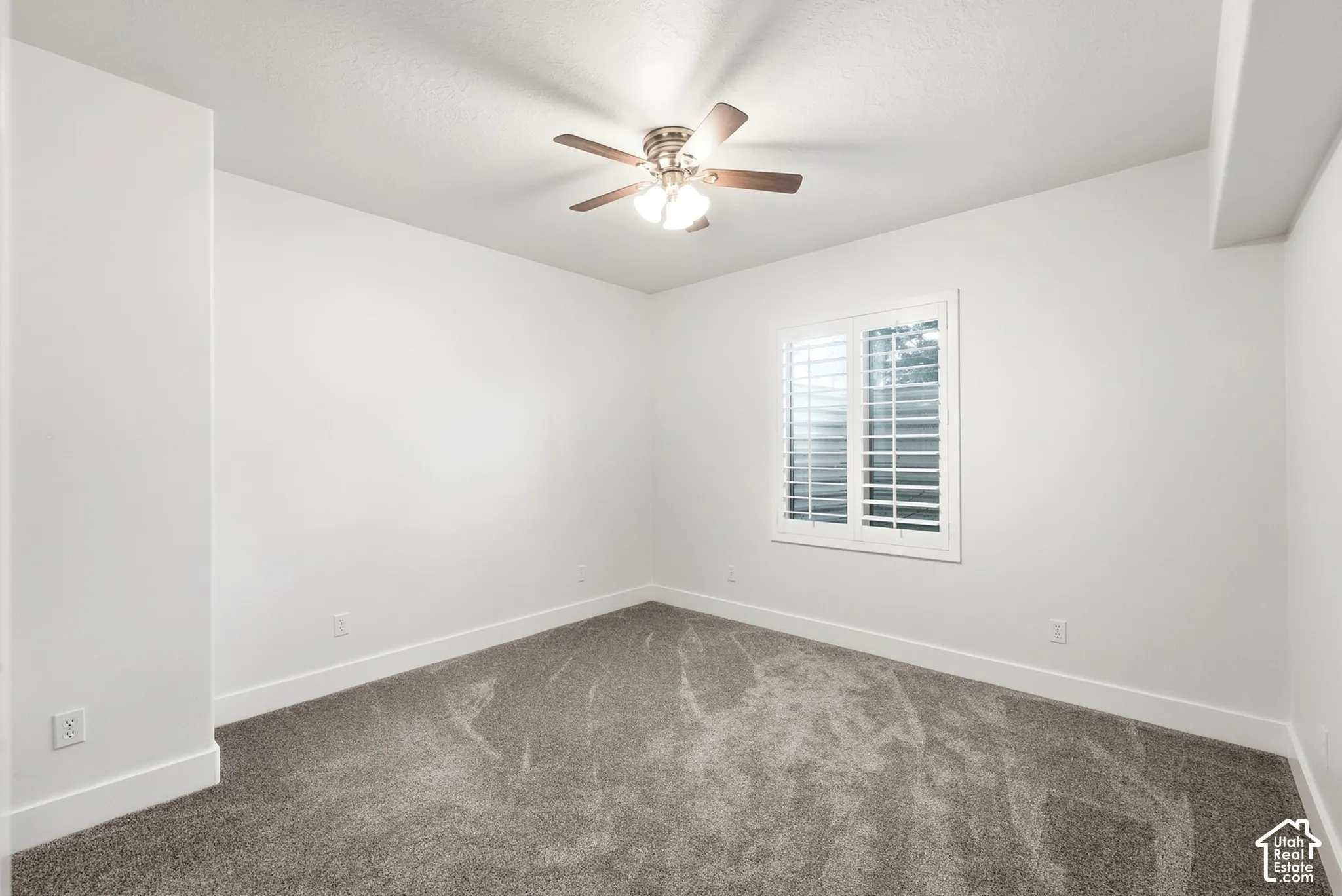 Neutral wall color, plush carpet flooring, ceiling fan with integrated lighting, and window with plantation shutters