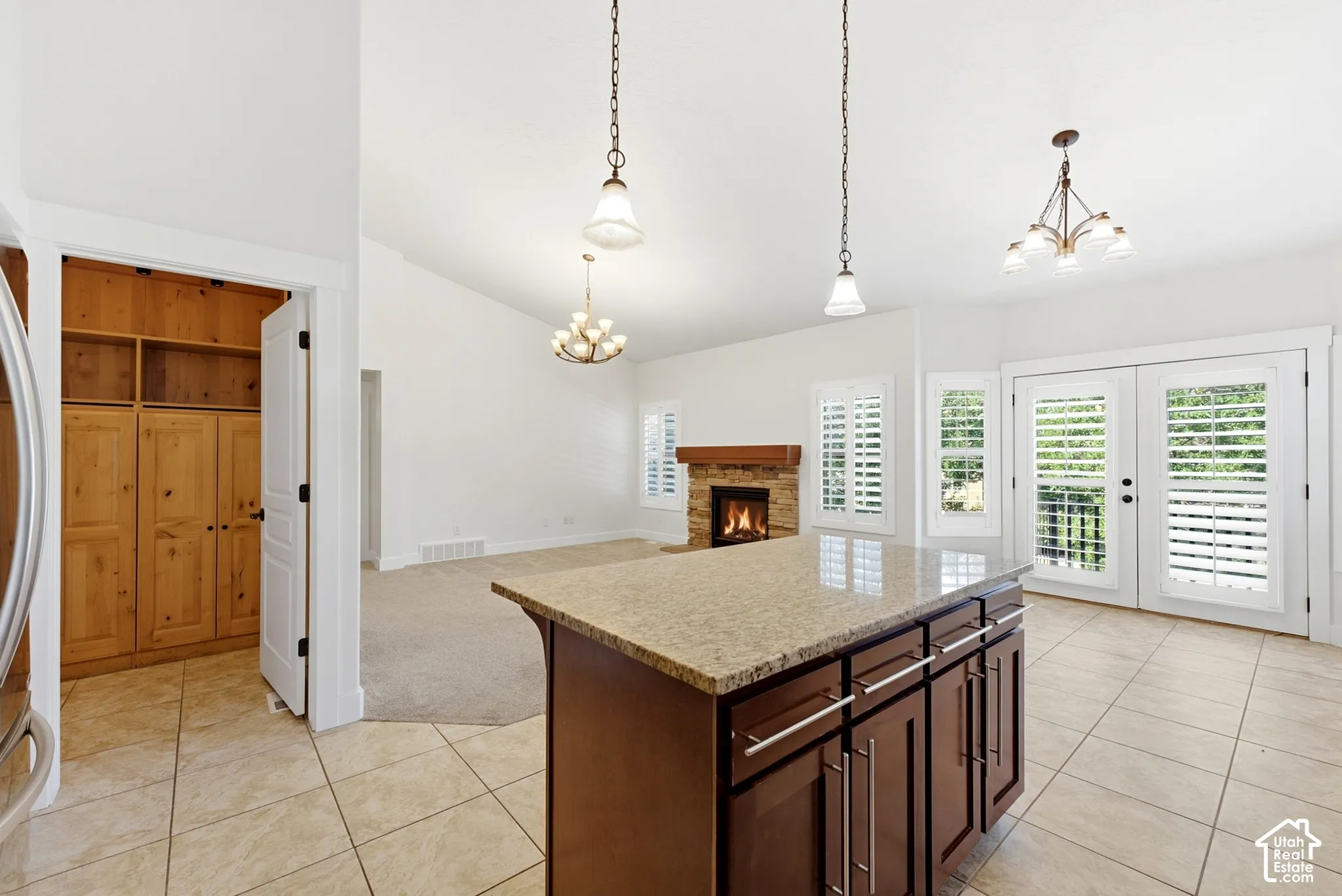 Kitchen island with stone-finish countertop, tile flooring, double French doors, wood-finish built-in pantry, and a stone-finish fireplace
