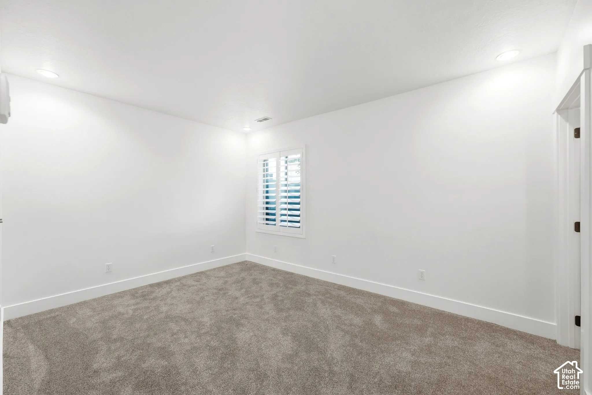 Neutral white walls, recessed ceiling lighting, textured carpet, and a window with white plantation shutters