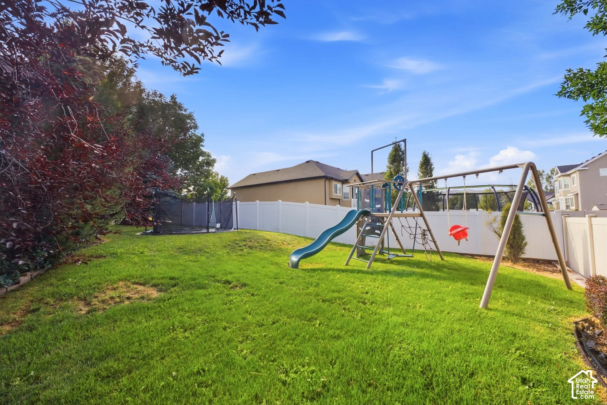 Expansive lawn area with a play structure featuring a slide and swing set, and mature perimeter trees