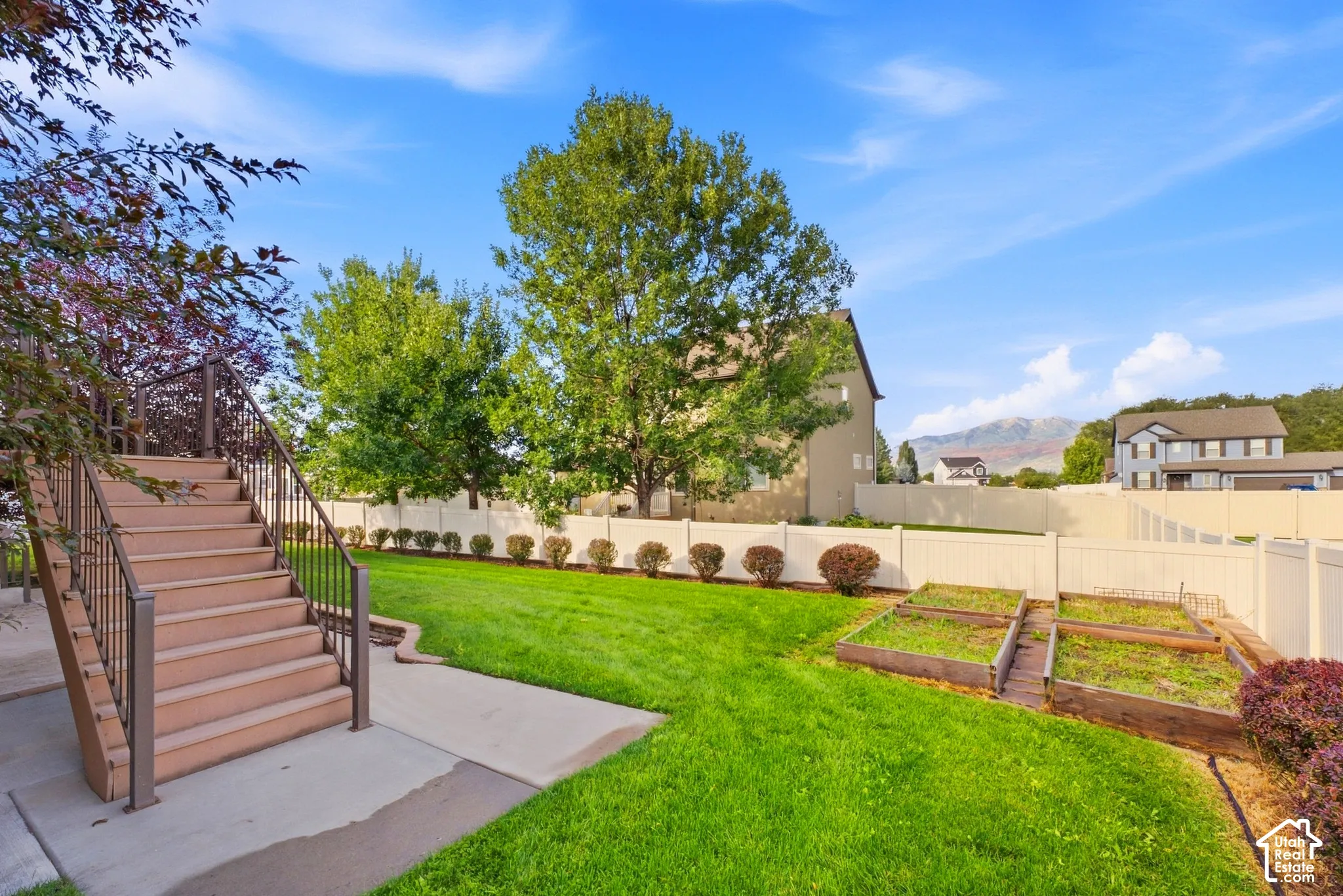Expansive manicured lawn with raised garden beds and a multi-level deck featuring metal railings