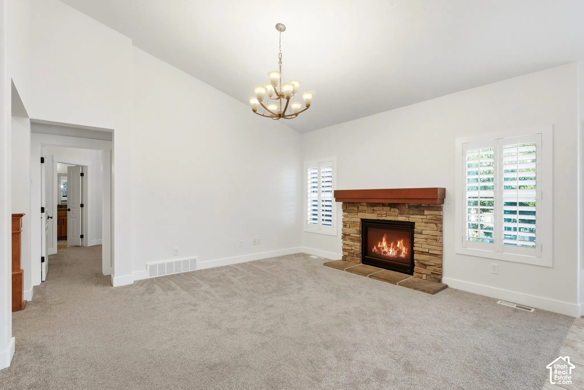 Vaulted ceiling with an ornate chandelier, stone-faced fireplace with a wood mantle, and plantation shutters