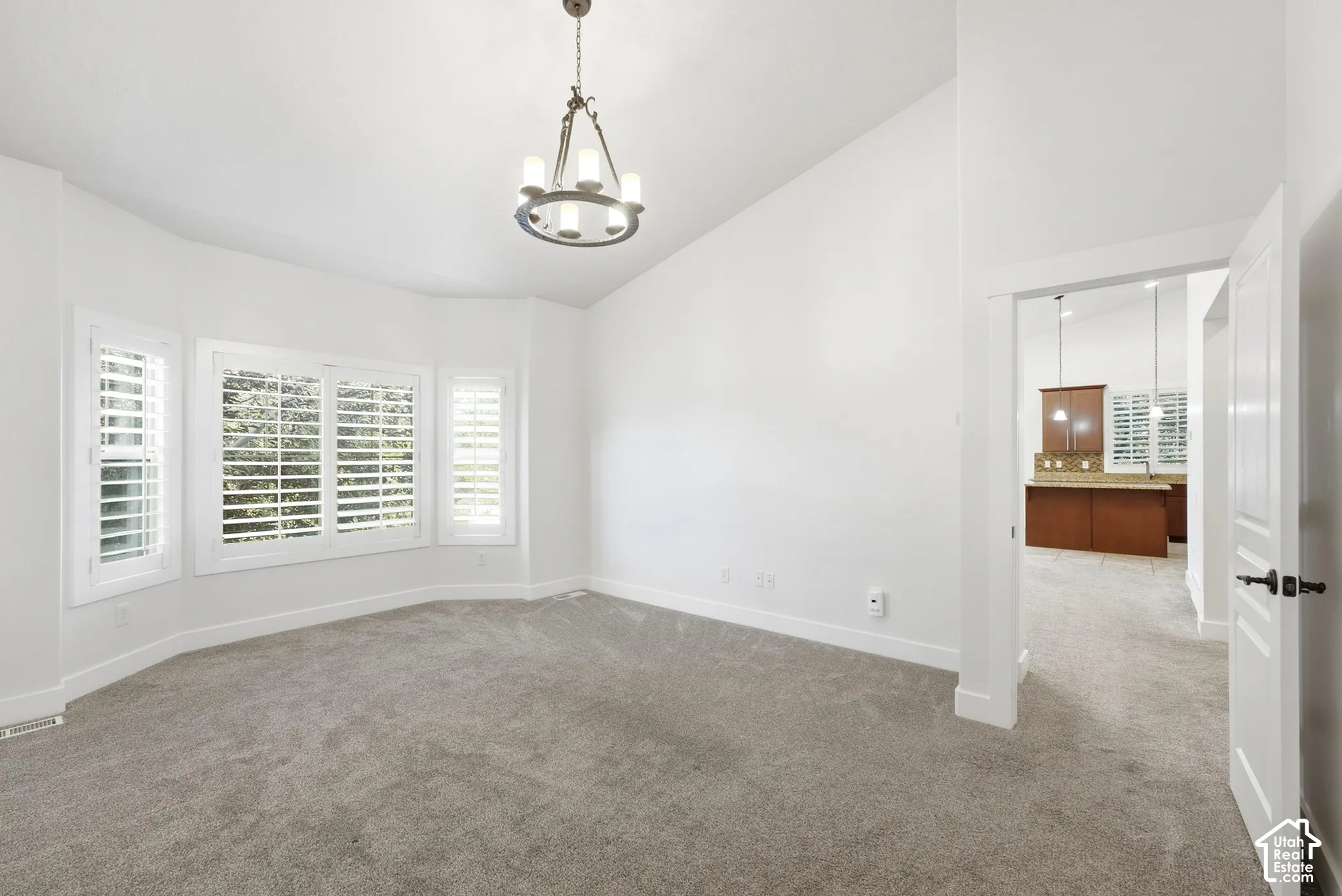 Recessed bay windows with plantation shutters, vaulted ceiling, neutral carpet flooring, and a chandelier lighting fixture