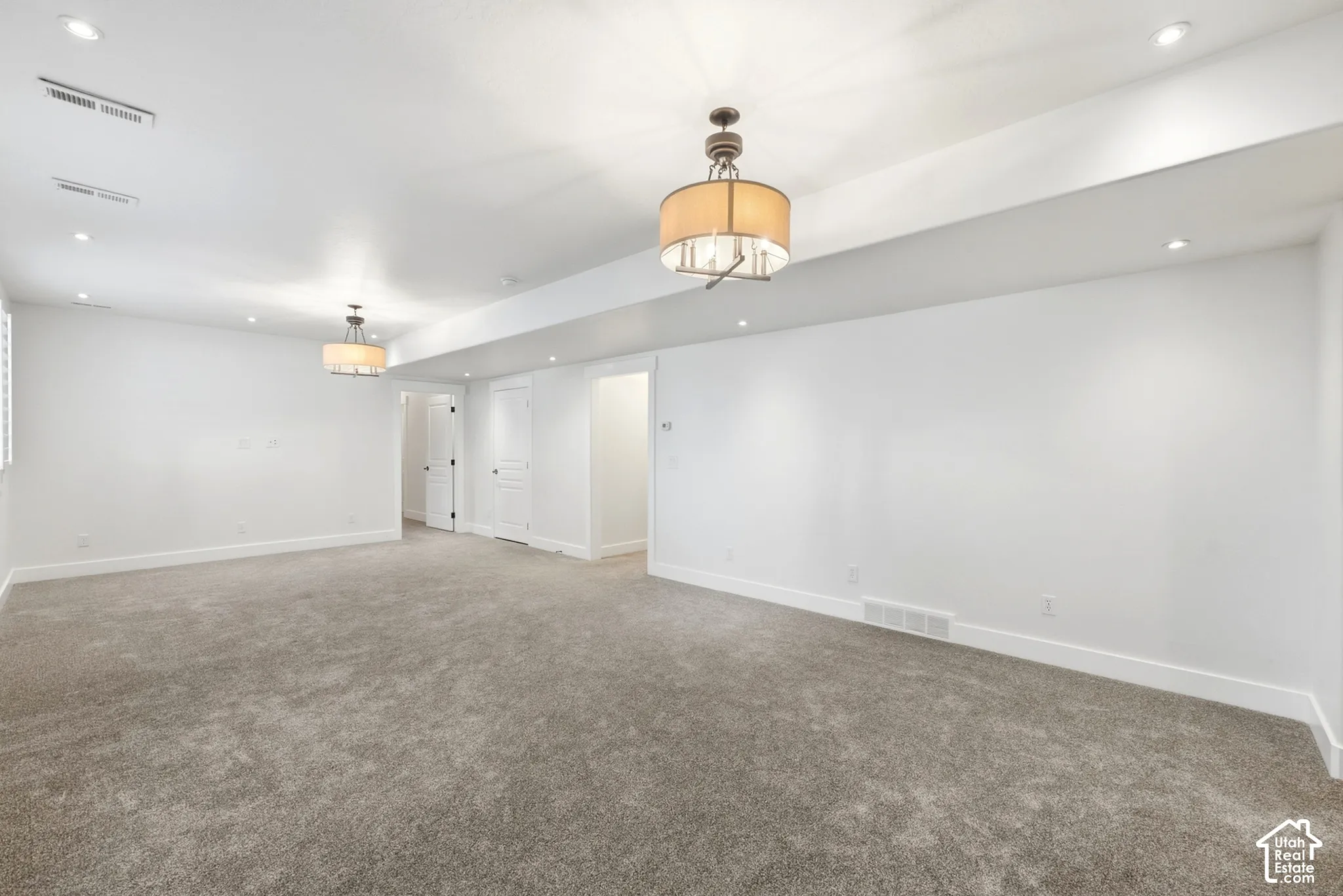 Spacious room featuring neutral carpeting, recessed lighting, and dual decorative ceiling fixtures