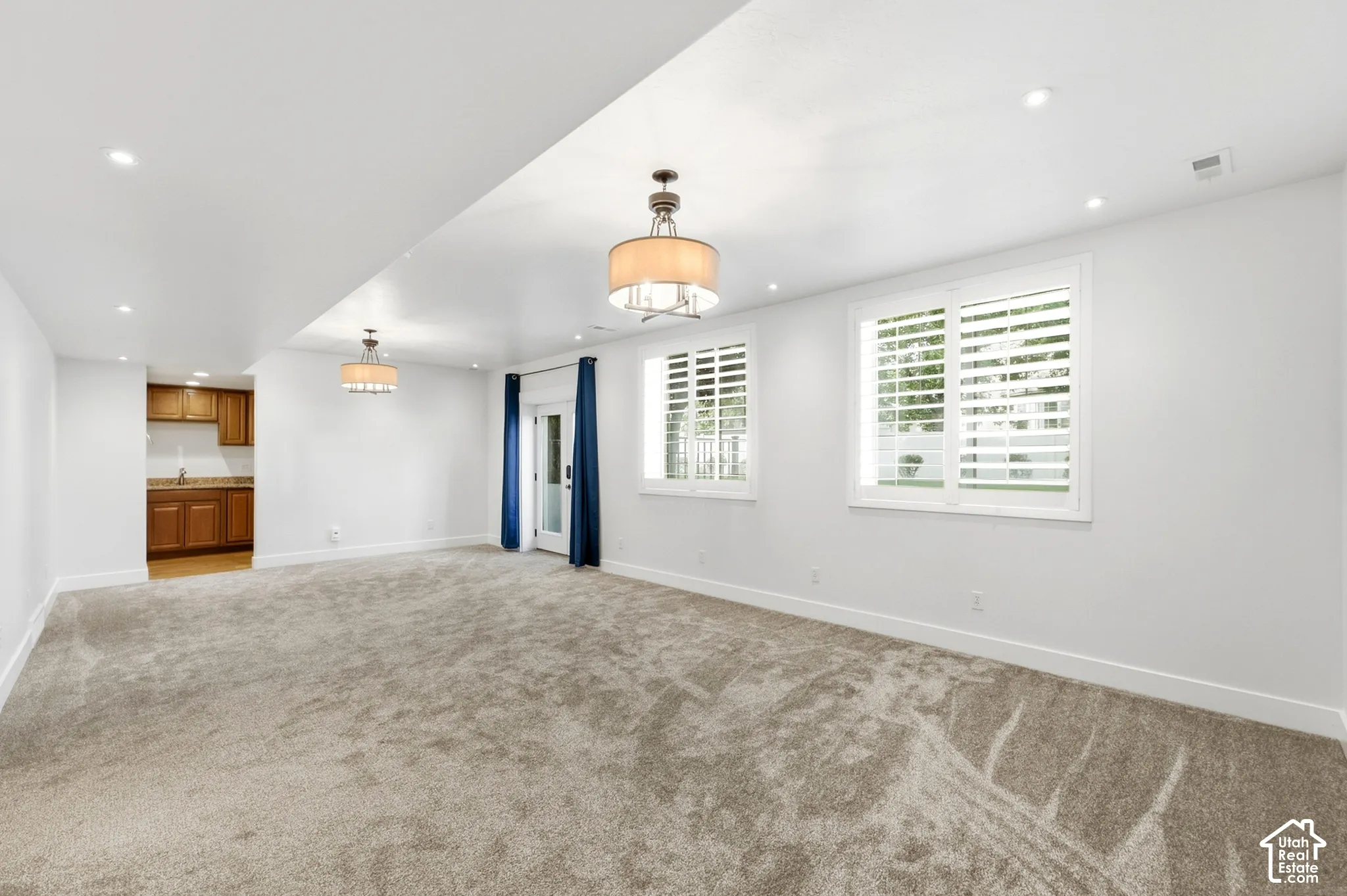 Spacious room featuring plush carpet, recessed lighting, two windows with plantation shutters, a glass-paned door, and a built-in wet bar with wood cabinetry