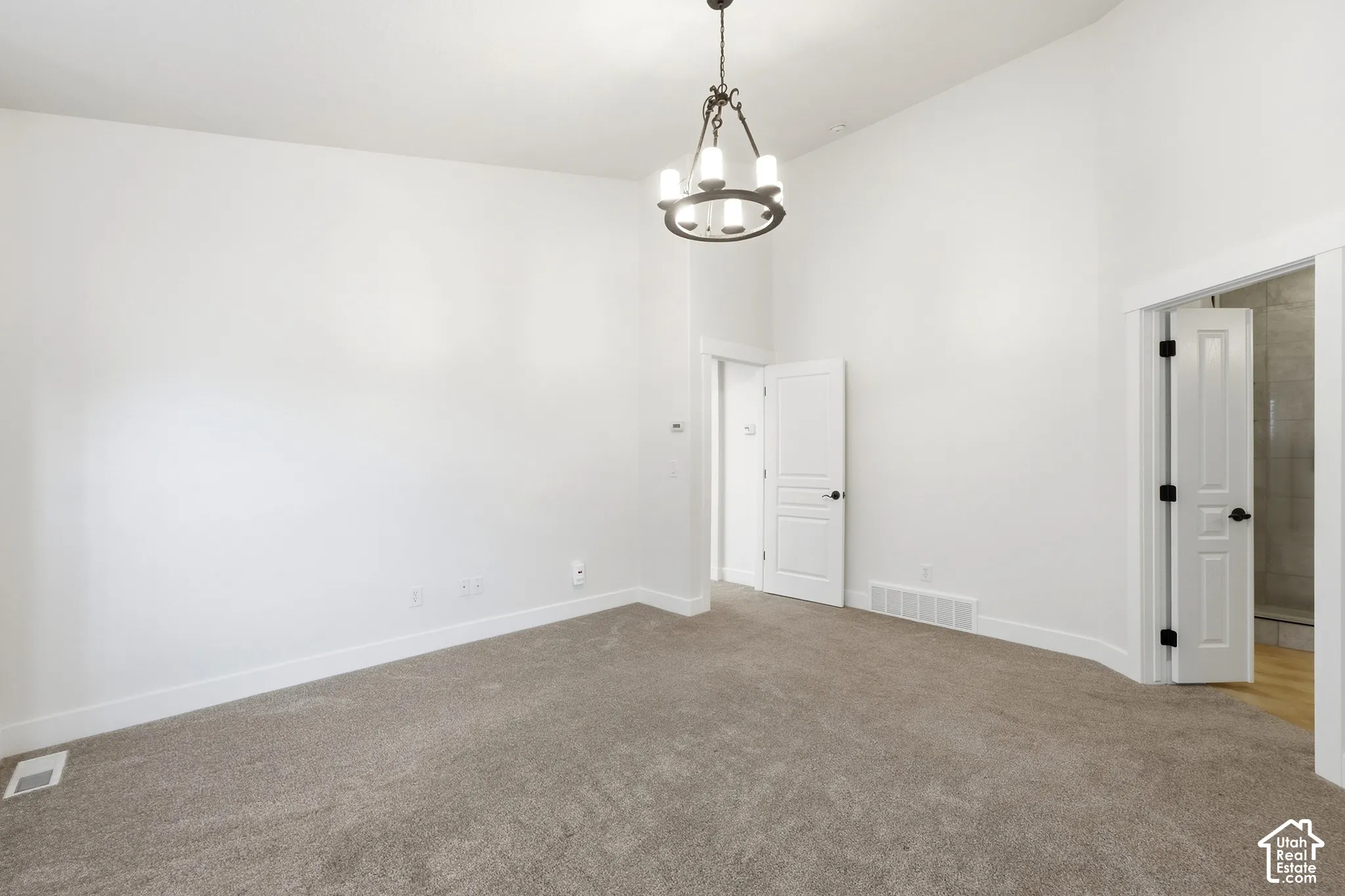 Vaulted ceiling featuring a decorative chandelier, white walls, and gray carpet flooring