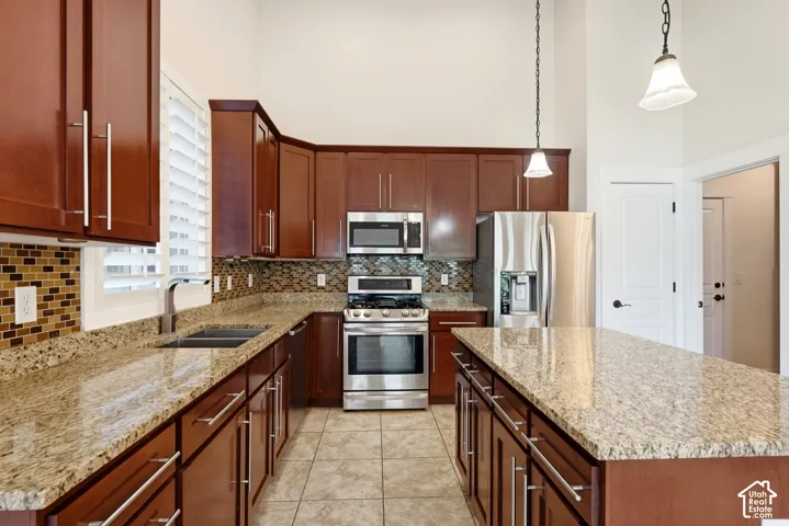 Kitchen featuring rich wood cabinetry, stainless steel appliances, granite countertops, an expansive center island, and tile flooring