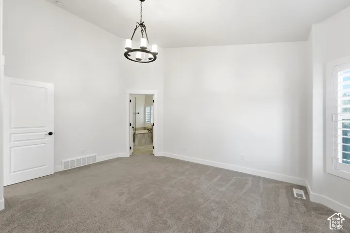 Plush carpeting, a modern chandelier, white interior shutters, and a white paneled door with black hardware