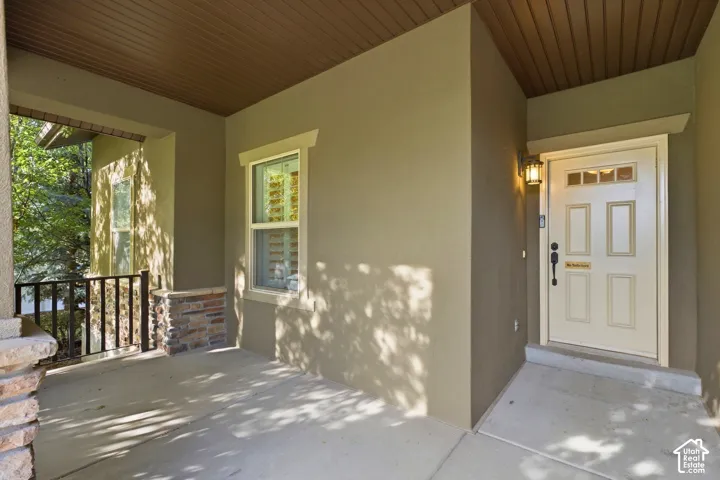 Covered porch entry featuring a wood-panel ceiling, sconce lighting, and a paneled entry door with transom windows