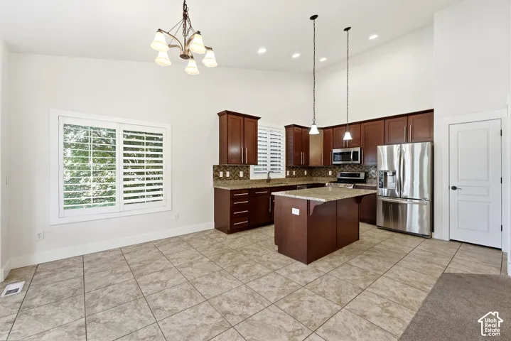 Vaulted ceilings with recessed lighting, tile flooring, rich wood cabinetry, stainless steel appliances, and a center island