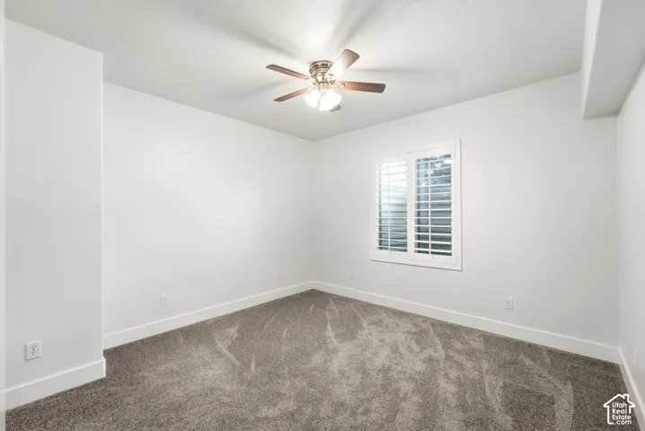 Neutral wall color, plush carpet flooring, ceiling fan with integrated lighting, and window with plantation shutters
