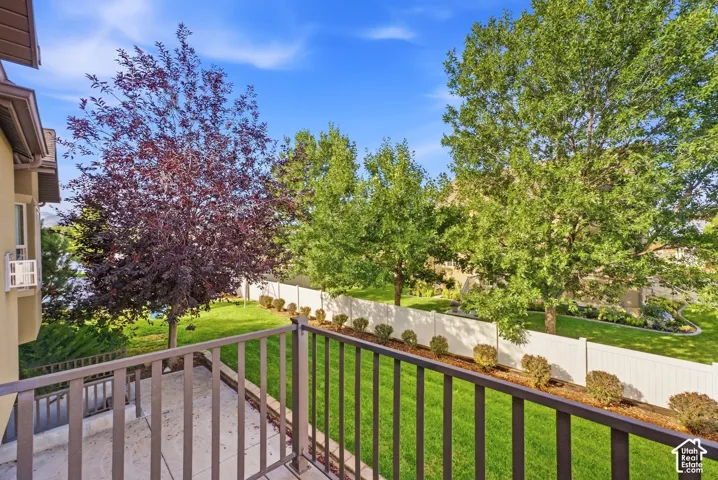 Balcony featuring metal railings and a concrete surface, overlooking a manicured lawn with mature trees and a privacy fence