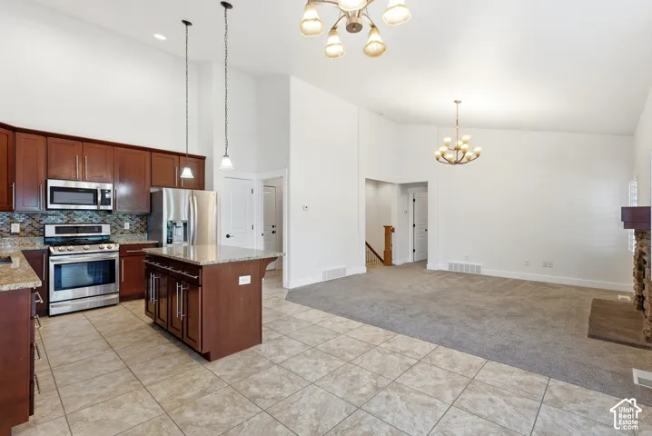Kitchen featuring stainless steel appliances, wood cabinetry, stone countertops, and tile flooring