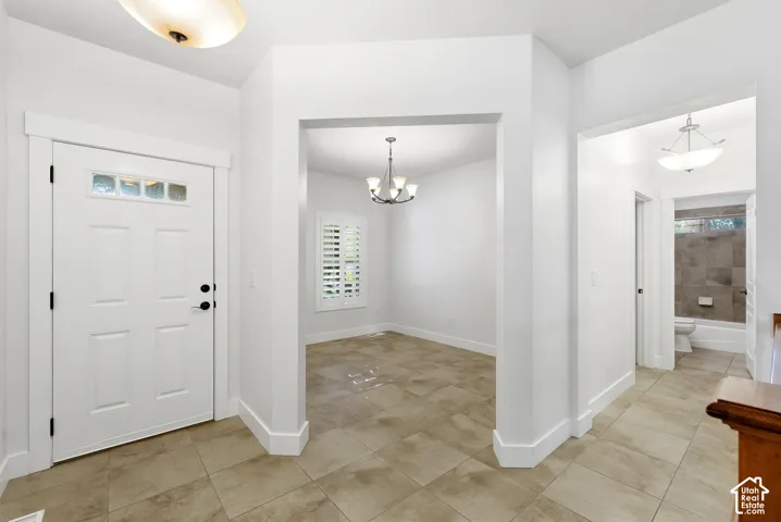 Entryway with tile flooring, a white paneled door with glass inserts, and a chandelier in an adjacent room