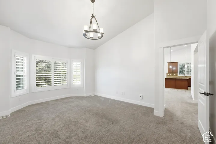 Recessed bay windows with plantation shutters, vaulted ceiling, neutral carpet flooring, and a chandelier lighting fixture