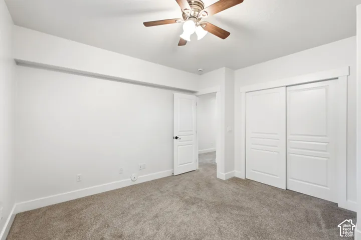 Neutral toned carpeting, white walls, and a ceiling fan with wood-finish blades