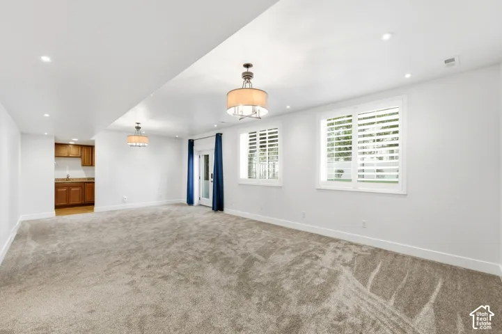 Spacious room featuring plush carpet, recessed lighting, two windows with plantation shutters, a glass-paned door, and a built-in wet bar with wood cabinetry