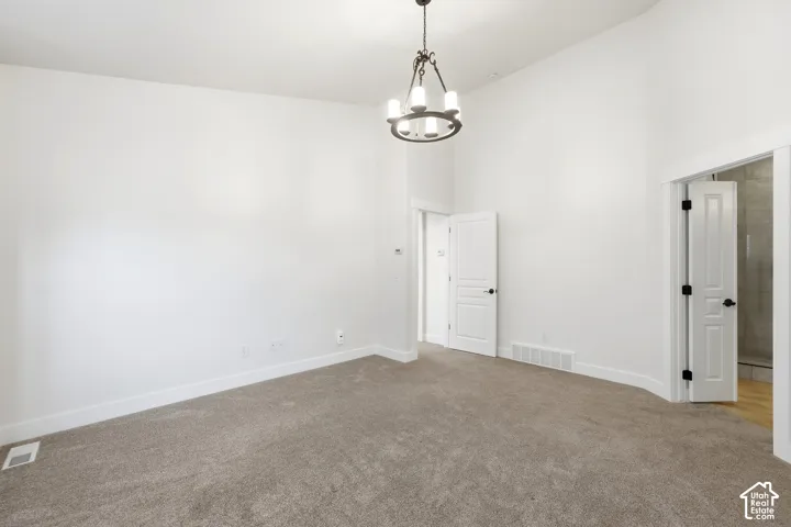 Vaulted ceiling featuring a decorative chandelier, white walls, and gray carpet flooring