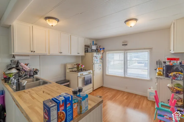 Kitchen featuring white cabinetry, a double basin sink, butcher block countertops, wood-finish flooring, and dual windows