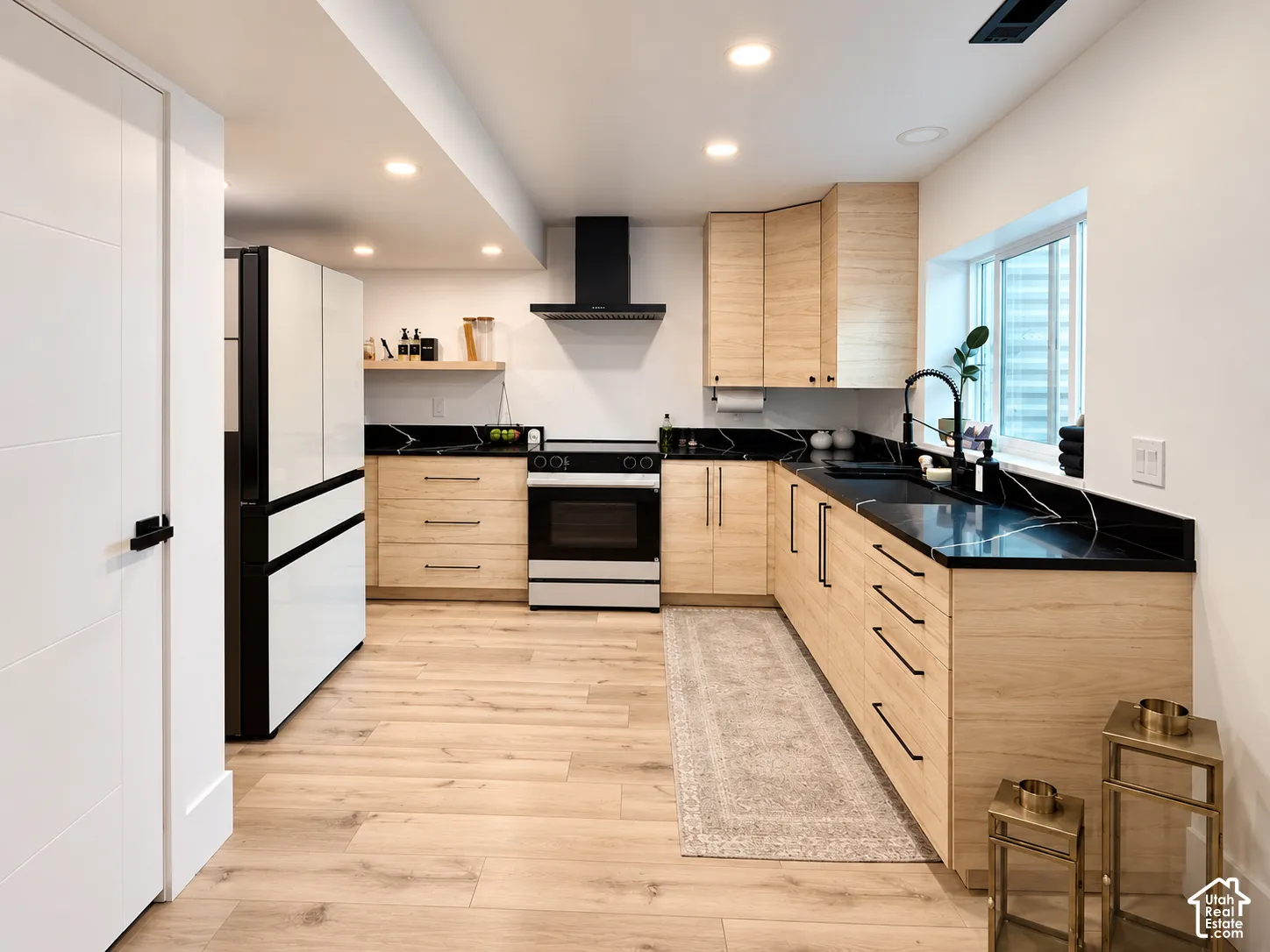 Kitchen featuring light wood-finish cabinetry, black countertops with white veining, integrated sink with a matte black faucet, stainless steel oven, and recessed lighting