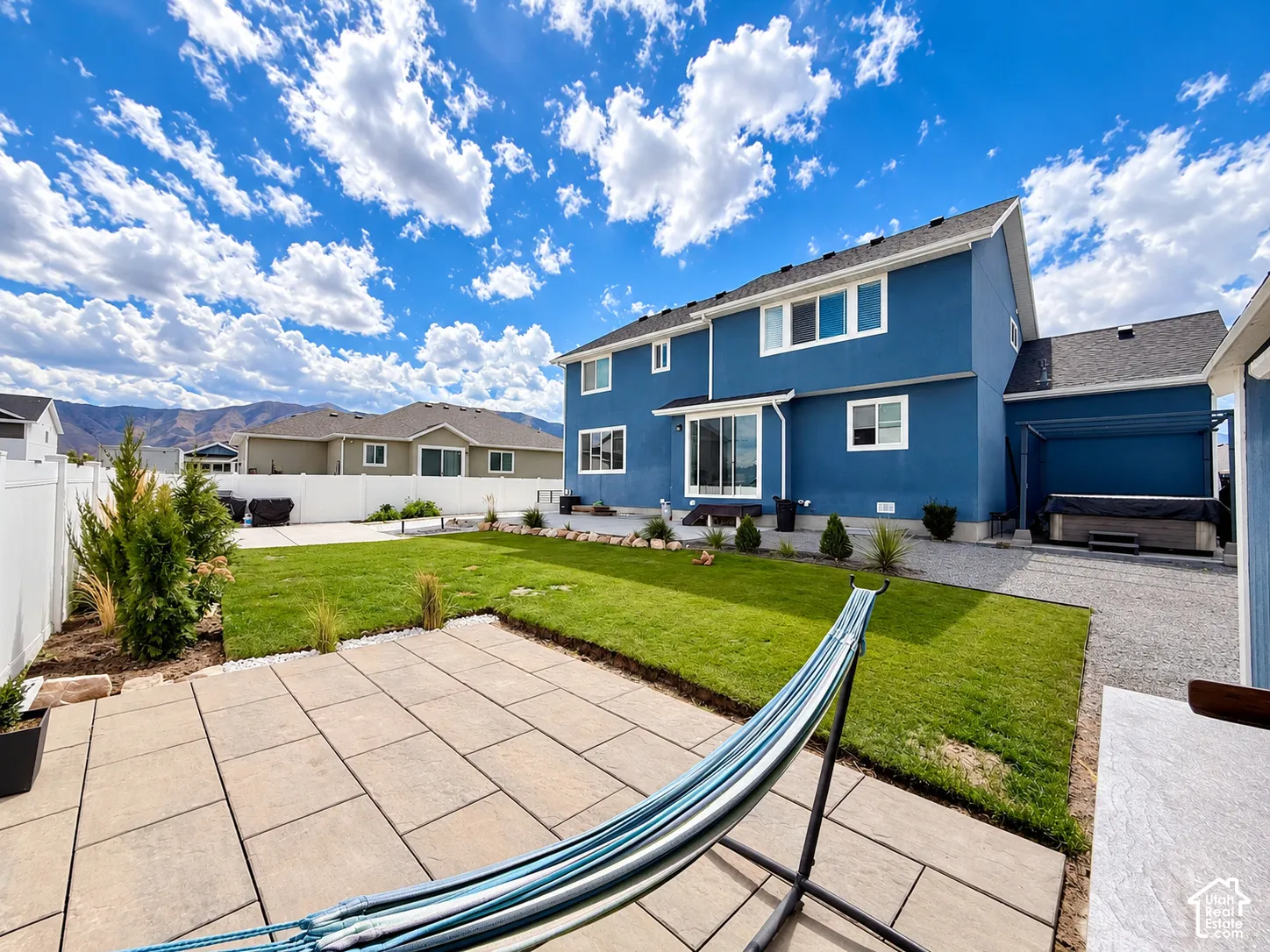 Rear exterior featuring a patio with large format pavers, a manicured lawn, and a privacy fence