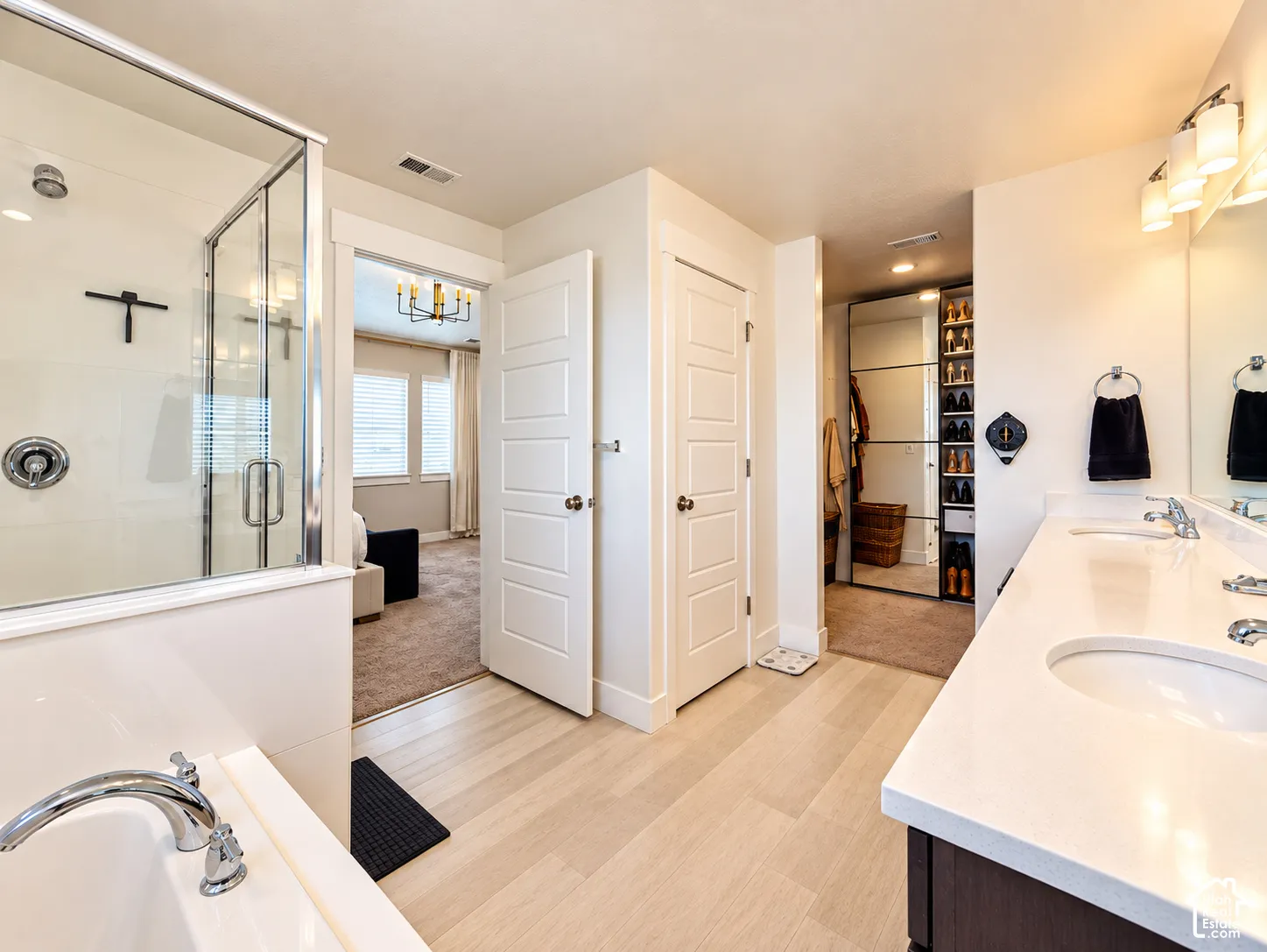 Spacious bathroom featuring a glass-enclosed shower, built-in soaking tub, a double vanity with ample counter space, and wood-finish flooring
