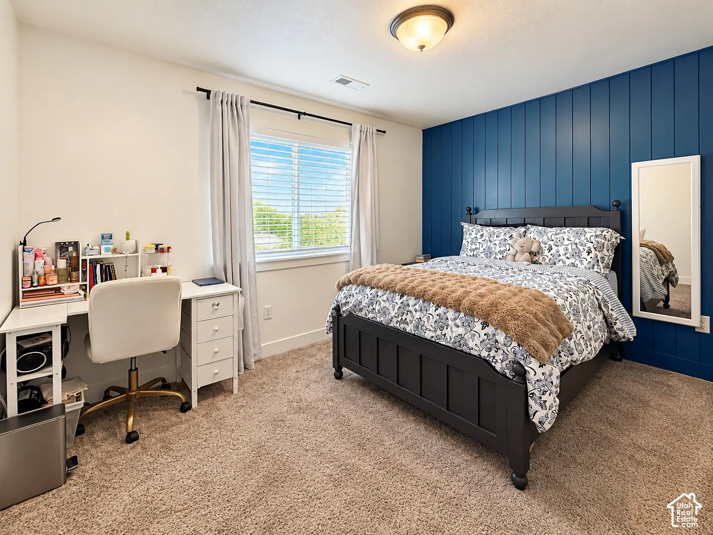 Plush carpet flooring, ceiling-mounted light fixture, window with blinds, and an accent wall with vertical paneling
