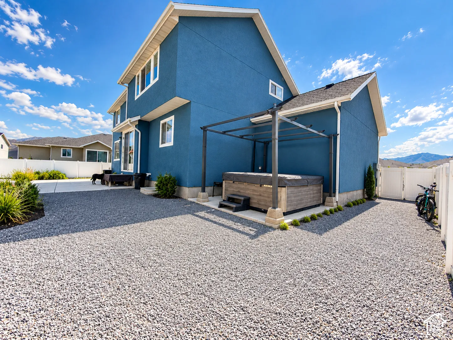 Expansive gravel landscaping, stucco exterior, hot tub with pergola, concrete patio, and white privacy fencing