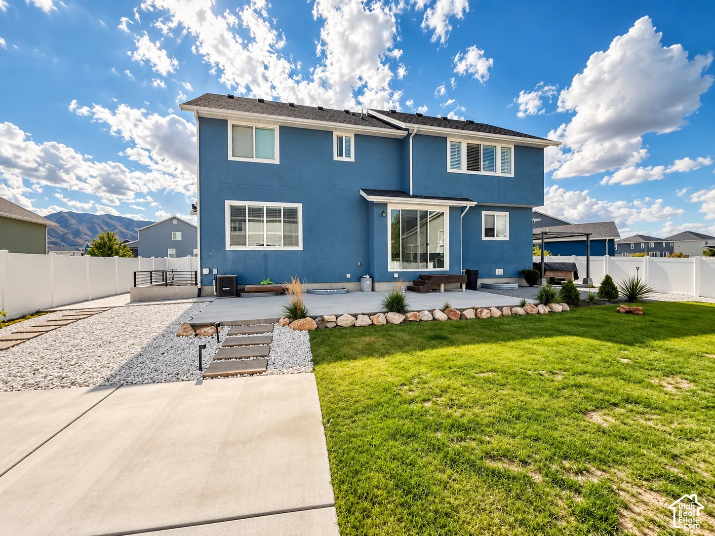 Expansive backyard featuring a manicured lawn, concrete patio, white privacy fencing, and mountain scenery