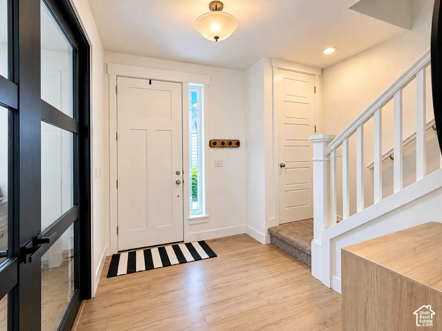 Entryway featuring wood-finish flooring, white panel doors, and a staircase with white balusters