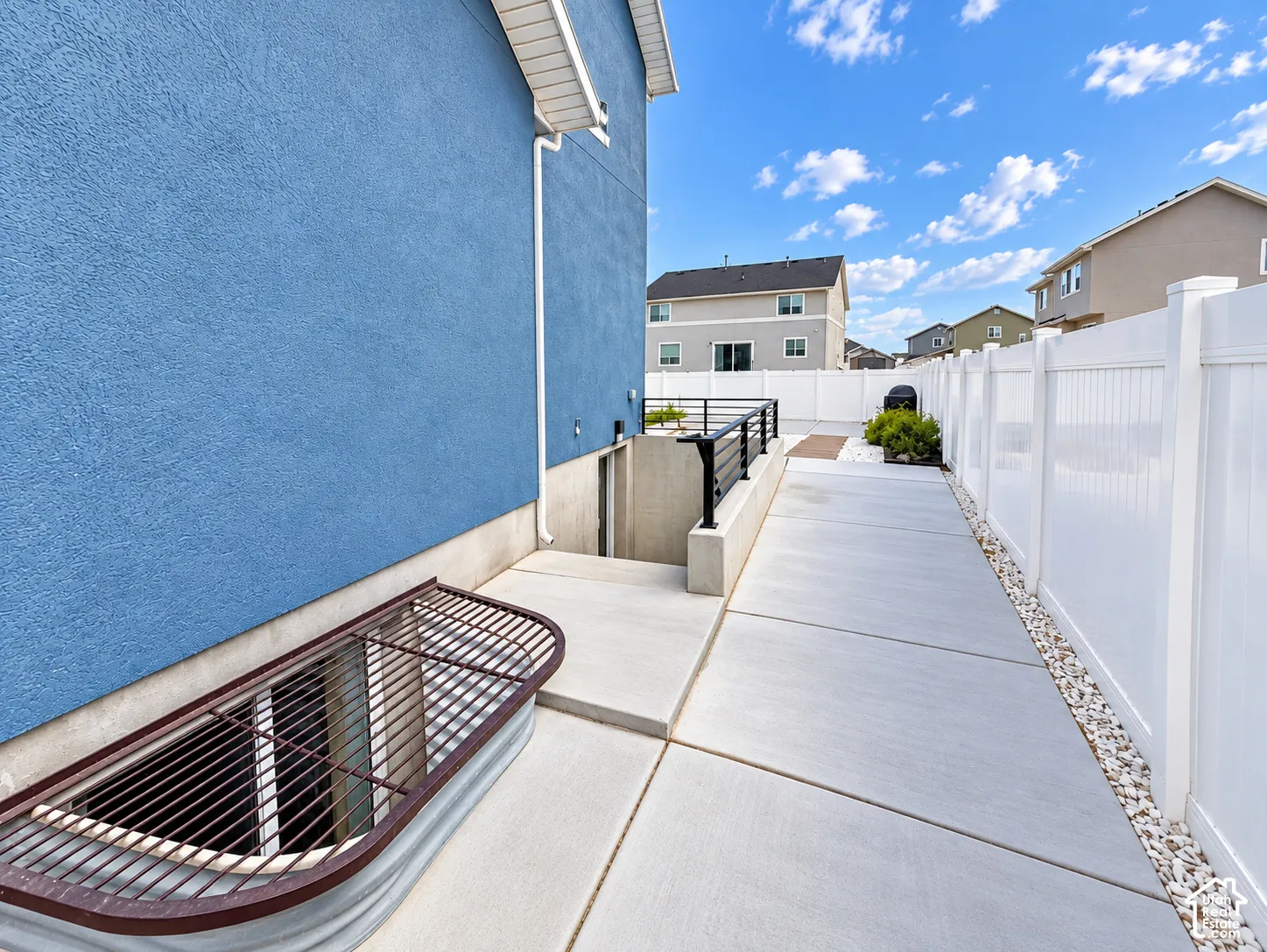 Stucco exterior with a window well, concrete walkway, and white privacy fencing