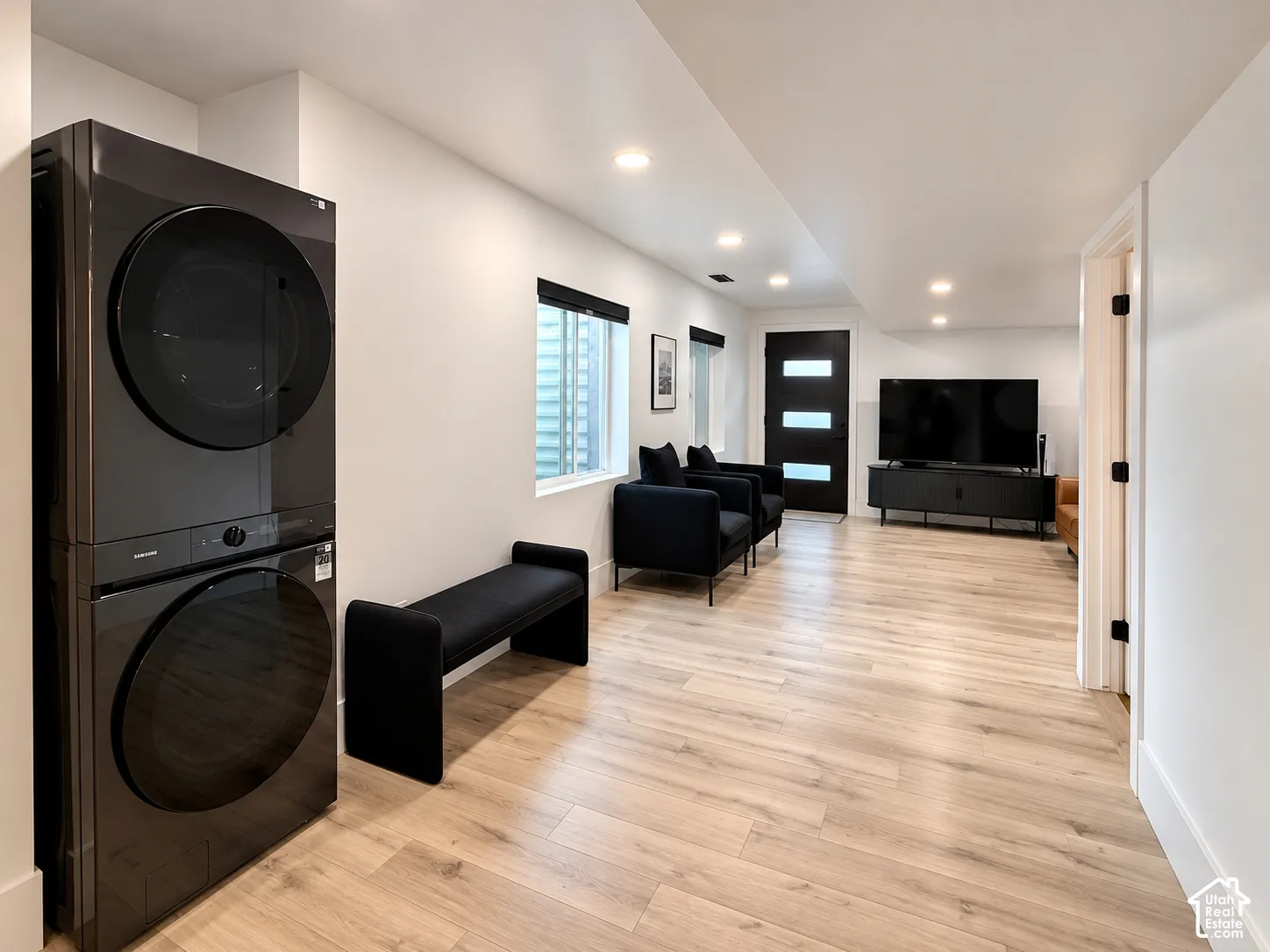 Stacked washer and dryer unit, wood-finish flooring, recessed lighting, and a modern exterior door with frosted glass inserts
