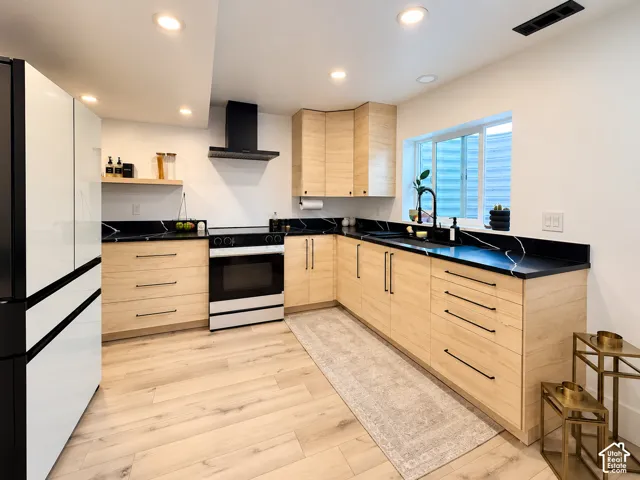 Modern kitchen featuring light wood-finish cabinetry, black countertops with white veining, wood-finish flooring, and recessed lighting