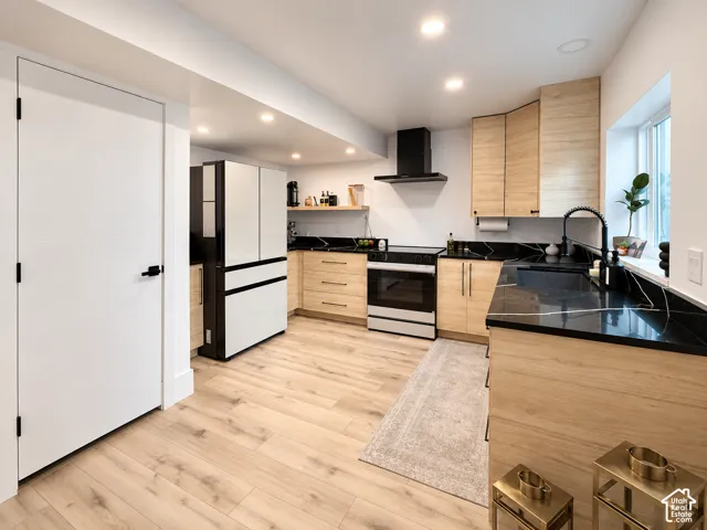 Modern kitchen featuring wood-finish cabinetry, black countertops with white veining, wood-finish flooring, recessed lighting, and a black range hood