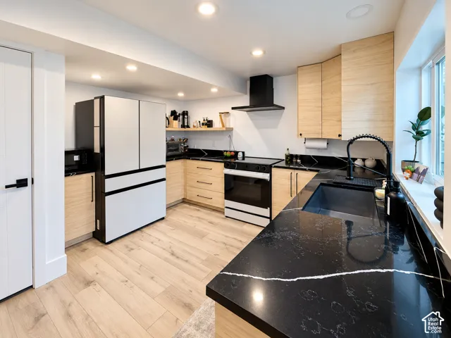 Modern kitchen featuring black countertops with white veining, light wood-finish cabinetry, stainless steel appliances, and light wood-finish flooring