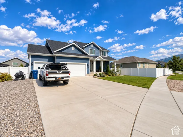 Blue siding exterior with white trim, a dark shingle roof, an attached two-car garage, concrete driveway, and a white privacy fence