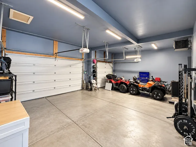 Spacious garage featuring two overhead doors, overhead fluorescent lighting, concrete flooring, and a wall-mounted utility heater