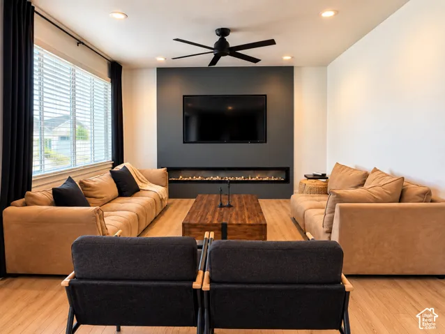Recessed lighting, wood-finish flooring, and a linear fireplace with a dark accent wall