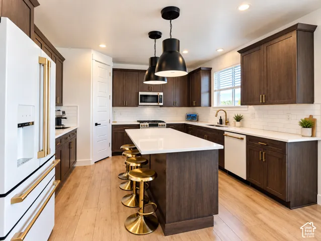 Spacious kitchen featuring wood-finish flooring, dark wood cabinetry with gold-tone hardware, white countertops, and a white subway tile backsplash