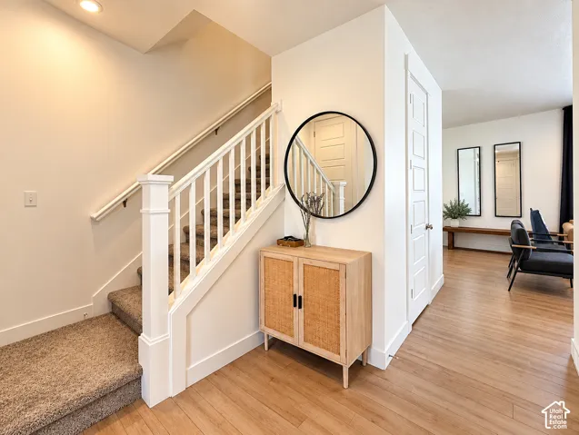 Staircase featuring white balusters and a carpeted tread, accompanied by wood-finish flooring and a contemporary white door with paneling