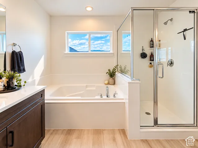 Soaking tub with chrome fixtures, glass-enclosed shower, wood-finish flooring, dark wood-finish vanity with white countertop, and recessed lighting
