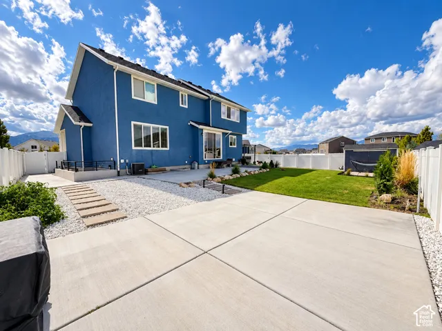 Expansive concrete patio area with a manicured lawn, white privacy fencing, and a gravel-bordered stepping stone pathway