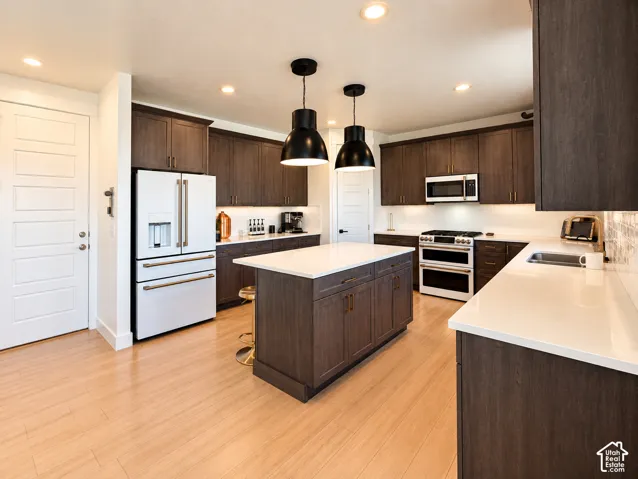 Kitchen featuring wood-finish cabinetry, white countertops, built-in stainless steel appliances, and a central island with pendant lighting