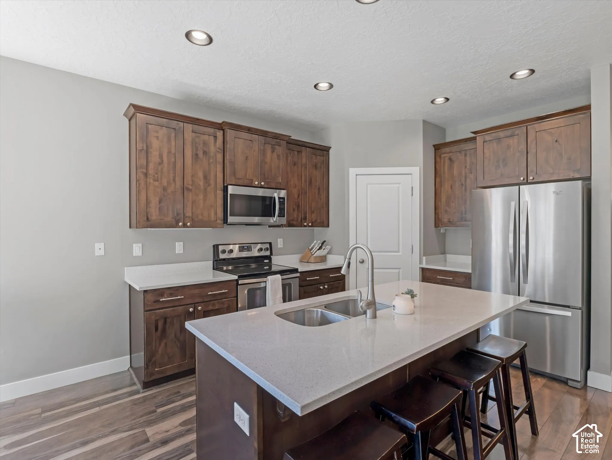 Kitchen featuring recessed lighting, wood-finish flooring, stainless steel appliances, dark wood cabinetry, and light-toned countertops