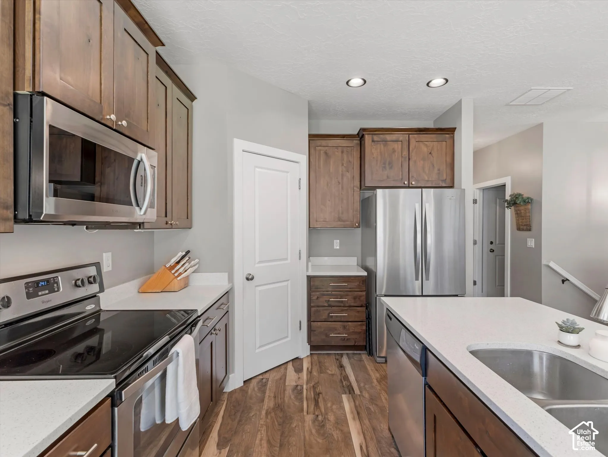Kitchen featuring wood-finish cabinetry, stainless steel appliances, white countertops, and wood-finish flooring